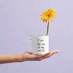 Hand hält Tasse mit Zitat „I am the hero of my own life“ und gelber Blume – Symbol für Selbstermächtigung bei Rosmary WEISS, Kinesiologin in Unterägeri