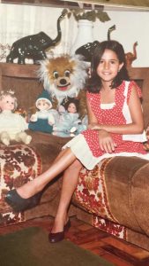 Rosmary WEISS als Kind im Jahr 1980 – ein Blick in die lebensfrohe Kindheit mit Puppen, Farben und Lächeln